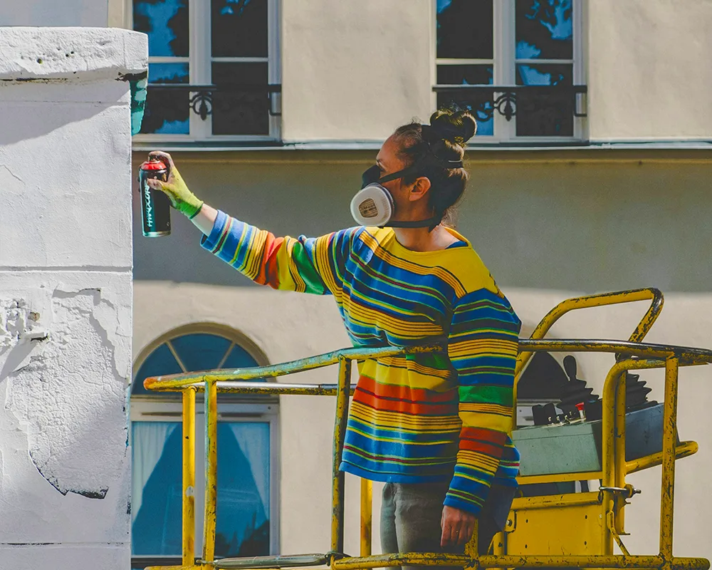 Woman on cherry picker uses spray can for street art project